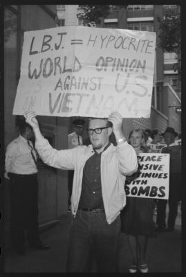 Protester holds placard saying "LBJ = Hypocrite. World opinion is against US in Vietnam."