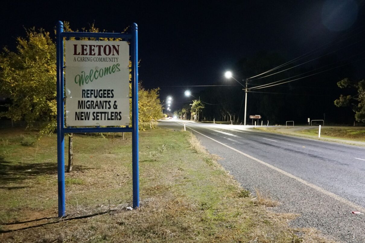 Sign by an empty country road reading "Leeton welcomes refugees, migrants & new settlers. A caring community."